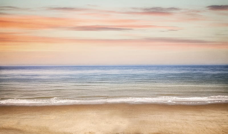 Calm ocean waves beneath a soft coral sky